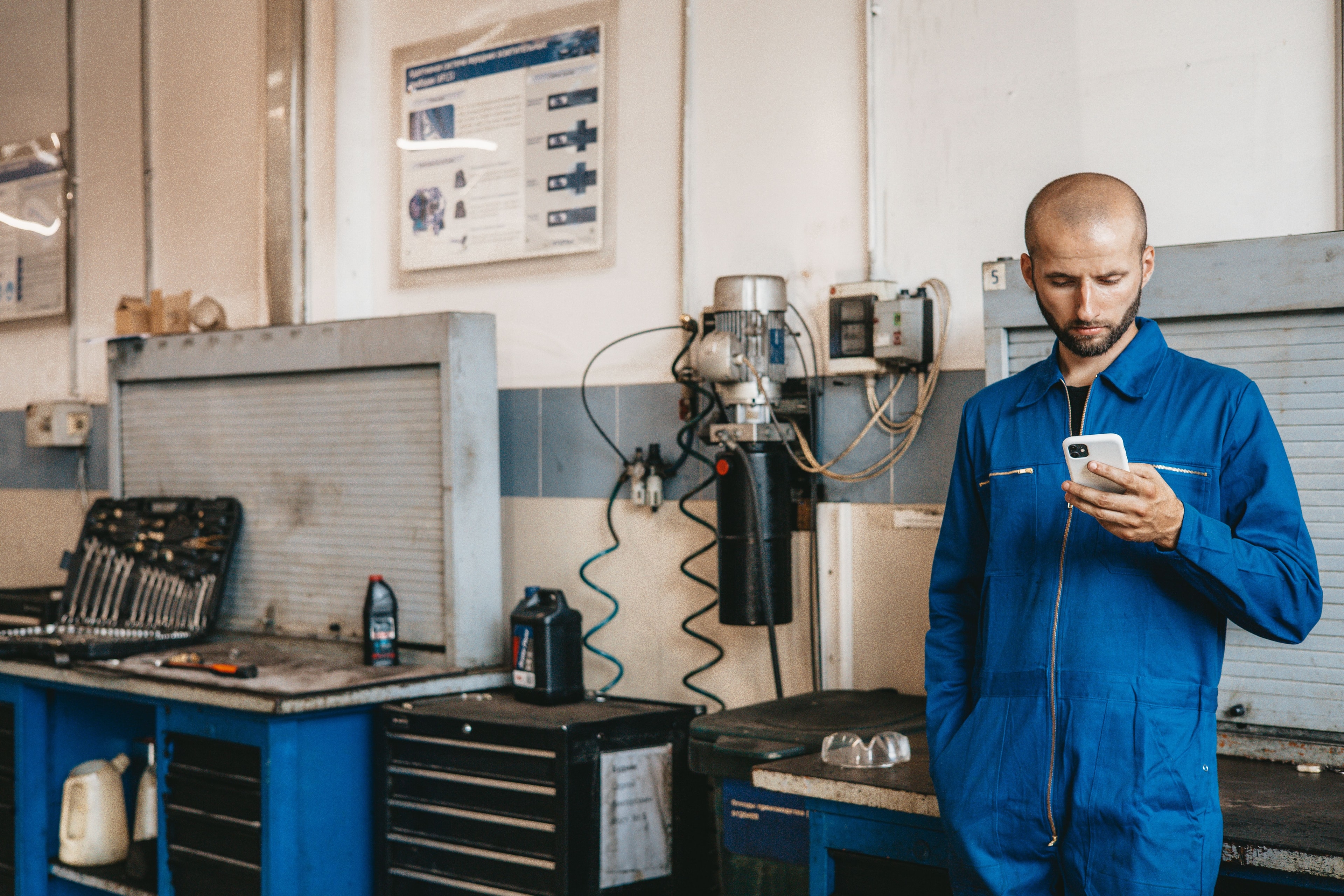 Mechanic in blue overalls checking his phone in a workshop